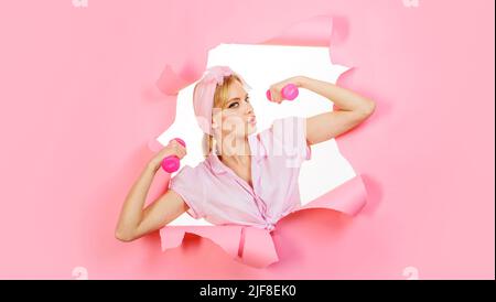 Fitnesstraining. Sportliches Mädchen mit Hanteln schauen durch Papier. Frau Athletin mit Sportausrüstung. Stockfoto