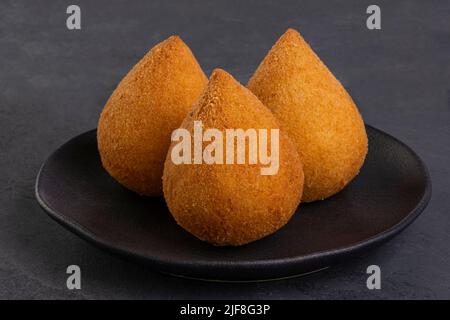 Traditioneller gebratener Coxinha auf einem schwarzen Teller auf Schiefergrund - brasilianischer Snack. Stockfoto