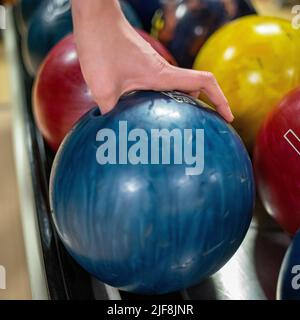 Eine Nahaufnahme einer Hand, die eine blaue Bowlingkugel aufgreift Stockfoto