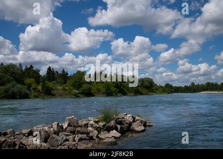 Weite szenische Aufnahme eines großen Flusses, der in Deutschland fließt, der Lech. Am blauen Himmel sind viele weiße Wolken. Am Rande des Wassers sind viele Bäume. Stockfoto