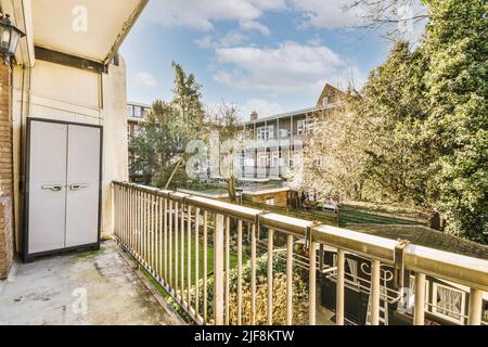 Enger Balkon mit Stuhl und TürPfeil Balkon mit weißem Geländer und Schrank mit Blick auf Backsteinhäuser und Innenhof Stockfoto