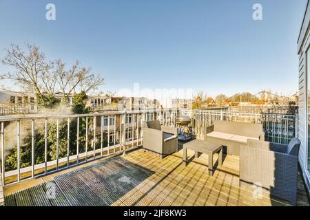 Graues Sofa mit Sesseln auf der Terrasse eines Mehrfamilienhauses mit Blick auf Ziegelhäuser Stockfoto