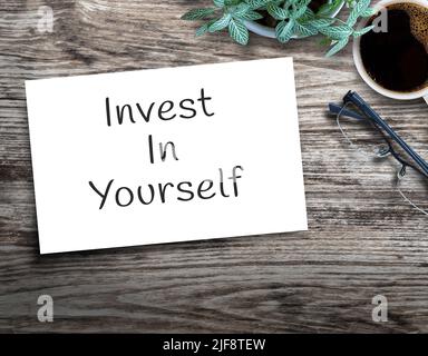 Text-Schild zeigt Invest in yourself. Auf Holztisch mit Blume, Gläser und Tasse Kaffee auf Holz Hintergrund in Büro-Arbeitsplatz. Stockfoto