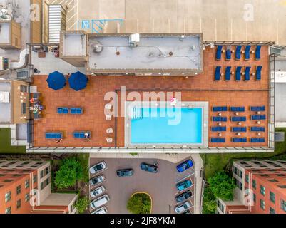 Luftansicht des Dachpools mit Reihen von blauen Liegestühlen, Grill, Bar auf einem luxuriösen Wohngebäude in der Innenstadt von East Coast in den USA Stockfoto