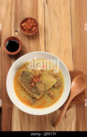 Gulai oder Gule Daging Kambing, indonesische traditionelle Ziegencurry-Suppe mit reichhaltigem Gewürz für das IED Al Adha-Menü. Draufsicht auf Holzhintergrund Stockfoto