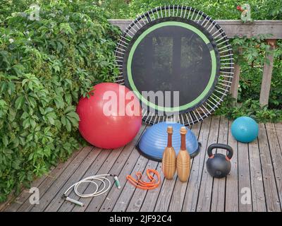 Home Gym Konzept - Slam und Schweizer Bällen, bosu Ball, Eisen Kettlebell, Mini-Trampolin, schweres Springseil, Widerstandsband und hölzerne indische Clubs auf einem Stockfoto