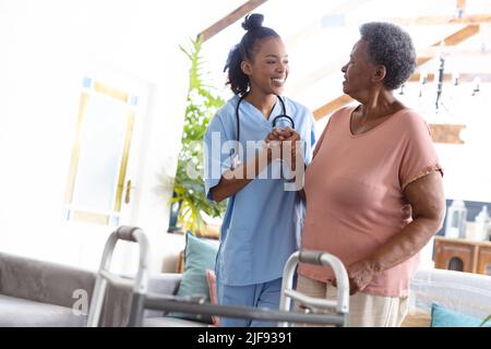 Lächelnder afroamerikanischer Arzt, der die Hand eines älteren Patienten hält, während er zu Hause steht und Platz kopiert Stockfoto