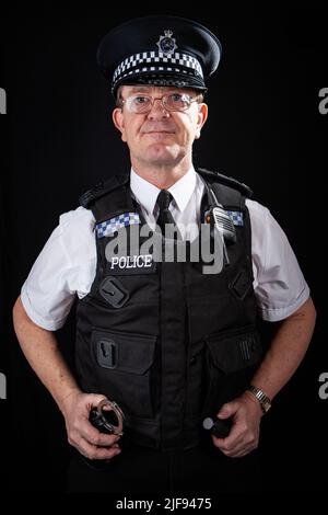 Ein britischer uniformierte Polizist alarmiert und bereitet sich auf den Dienst vor. Teil einer Serie von Bildern mit demselben Zeichenmodell. Stockfoto