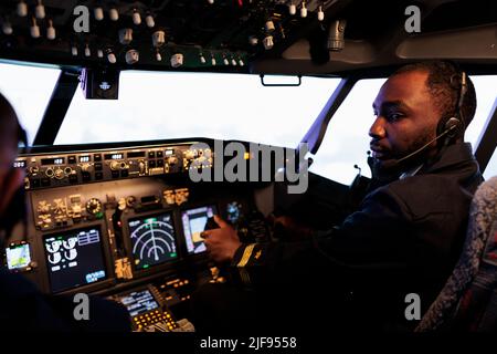 afroamerikanischer Flieger, der in Teamarbeit mit dem Kapitän ein Flugzeug fliegt, mit Dashboard-Befehl und Navigation. Ein Team von Flugzeugen drückt die Tasten des Bedienfelds und den Hebel, um abzuheben und zu fliegen. Stockfoto