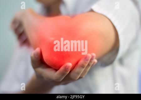 Schmerzen im Ellenbogengelenk des jungen südostasiatischen Mannes. Konzept von Ellenbogenschmerzen, rheumatoider Arthritis und Armproblemen. Stockfoto