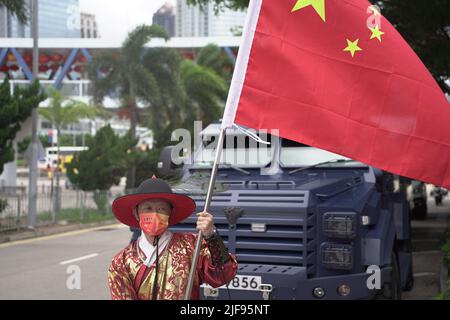 Menschen in einer feierlichen Prozession posieren mit einer chinesischen Flagge in der Nähe eines gepanzerten Fahrzeugs der Polizei. Xi Jinping, der chinesische Führer, ist heute in der SAR-Stadt, um an der Zeremonie zum Übergabejubiläum 25. teilzunehmen, sowie an der Vereidigung des neuen Chefs von Hong Kongs, John Lee. Stockfoto