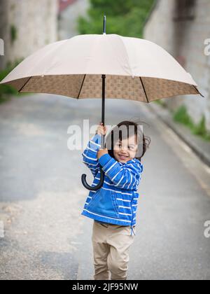 Kleiner, im Osten schöner Junge, der draußen mit einem Regenschirm spielt Stockfoto