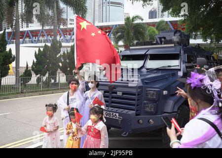 Menschen in einer feierlichen Prozession posieren mit einer chinesischen Flagge in der Nähe eines gepanzerten Fahrzeugs der Polizei. Xi Jinping, der chinesische Führer, ist heute in der SAR-Stadt, um an der Zeremonie zum Übergabejubiläum 25. teilzunehmen, sowie an der Vereidigung des neuen Chefs von Hong Kongs, John Lee. Stockfoto