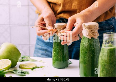 Eine Frau schließt Pakete mit frisch zubereiteten Smoothies aus grünem Gemüse und Obst Stockfoto