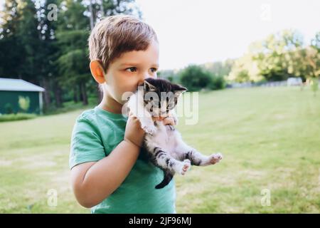 Kleines Kind küsst ein Kätzchen in seinen Armen in der Natur Stockfoto