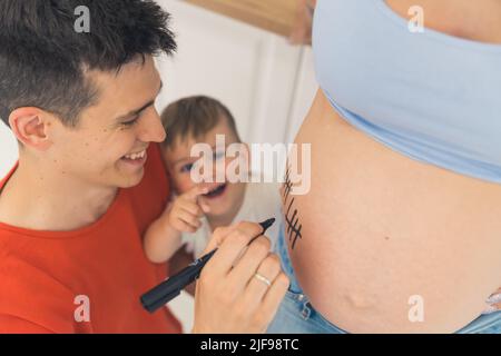 Glückliche Familie Zählen Schwangerschaftswochen zusammen und bilden Linien auf dem Bauch der Schwangeren. Hochwertige Fotos Stockfoto