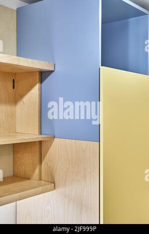 Fragment von Sperrholz Bücherregalen und gelb-blauen Sperrholzschrank zu Hause. Moderne Haushaltsmöbel für Schlafzimmer Innenansicht Stockfoto