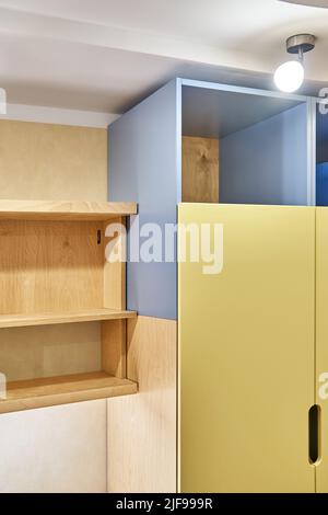 Fragment von Sperrholz Bücherregalen und gelb-blauen Sperrholzschrank zu Hause. Moderne Haushaltsmöbel für Schlafzimmer Innenansicht Stockfoto