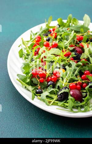 Sommer köstlicher Salat mit Rucola und frischen Beeren, roten und schwarzen Johannisbeeren, süßen Kirschen und schwarzen Maulbeeren, Salat auf einem ovalen weißen Teller Stockfoto