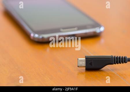 Nahaufnahme des Ladevorgangs von Smartphones mit anschliesdem USB-Kabel Holzstruktur Hintergrund Stockfoto