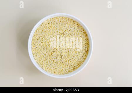 Rohe Risoni-Pasta in einer weißen Schüssel auf hellem Hintergrund. Das Konzept der traditionellen italienischen Küche. Horizontale Ausrichtung. Draufsicht. Kopierbereich. Stockfoto