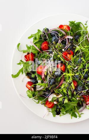 Leichter Salat mit Rucola und Beeren, Erdbeeren und Blaubeeren, köstlicher gesunder Sommersalat auf weißem Hintergrund Stockfoto