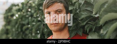 Portrait of Face harsch wütend unrasiert reifen 40+ Jahre Mann allein Reisenden mit Stoppeln und braunen Augen auf dem Hintergrund der grünen Bäume Pflanzen in der Natur Stockfoto