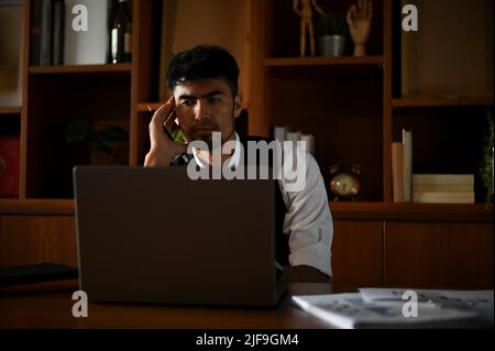 Seriöser asiatischer Geschäftsmann oder leitender Manager, der am Laptop-Computer arbeitet und an seinem Schreibtisch nach Plänen für Geschäftslösungen sucht Stockfoto