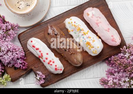 Eclair Dessert und Kaffee. Auf Holztisch mit Fliederblumen. Draufsicht flach liegend Stockfoto