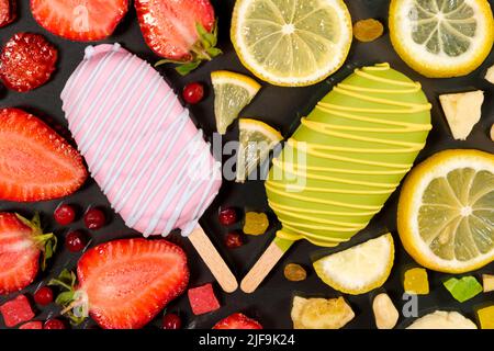 Zwei Eiscremes auf einem Stock - Erdbeere und Zitrone auf schwarzem Hintergrund. Sommerliche Fruchtdesserts. Stockfoto