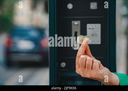 Frau, die Euro-Münzen vor dem Parkplatz hält. Stockfoto