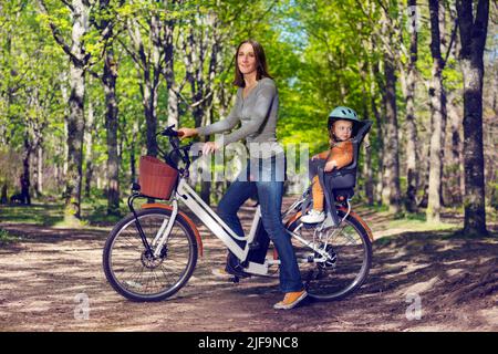 Frau und kleines Mädchen fahren Stadt Elektro-Fahrrad auf Parkallee Stockfoto