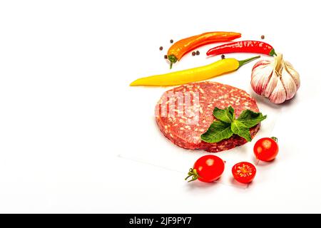 Rohe Steak-Koteletts aus Hackfleisch, isoliert auf weißem Hintergrund. Frisches Gemüse, Basilikum und Gewürze. Traditionelle Zutat für Burger, flach legen Stockfoto