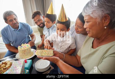 Gemischte Rennfamilie feiert Geburtstag und ist in der Lounge zu Hause Kuchen gekommen. Hispanische Verwandte genießen süße Kuchen und lächeln zu Hause Stockfoto