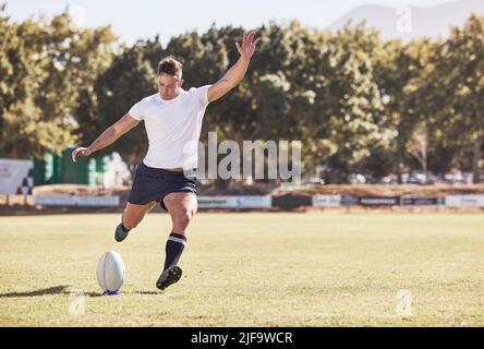 Ein kaukasischer Rugby-Spieler startet während eines Rugby-Spiels draußen auf dem Spielfeld. Junger Athletic Mann nimmt eine Strafe oder versucht, ein Tor Stockfoto