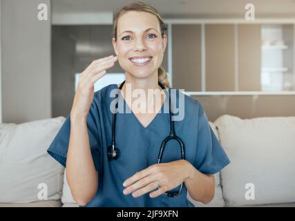 Ein schöner junger Arzt, der glücklich und freundlich aussieht, während er auf einem Sofa bei der Arbeit wartet. Lächelnder kaukasischer Mitarbeiter im Gesundheitswesen spricht und Hand verwendet Stockfoto