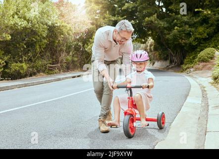 Ein glücklicher Vater lehrte sein kleines Mädchen, draußen mit dem Fahrrad zu fahren. Niedliches kaukasisches Kind trägt einen rosa Helm und radelt, während es sich mit ihrem Vater verklebt Stockfoto