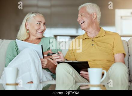 Glückliches älteres Paar, das seine Finanzen überprüft und den Ruhestand plant. Ältere kaukasische Männer und Frauen lächeln, während sie zu Hause planen und Papierkram machen Stockfoto