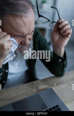 Aus der Perspektive eines bärtigen älteren Mannes, der eine Brille und ein zerknittertes Papier in der Nähe des Laptops hält Stockfoto