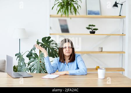 Junge Frau, die am Tisch sitzt und am Laptop arbeitet, verärgert Frau. Stockfoto