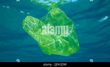 Plastikverschmutzung, Gelbe Plastiktüte schwimmt unter Wasser reflektiert auf der Oberfläche des blauen Wassers in Sonnenstrahlen. Plastikbeutel langsam entsorgen Stockfoto