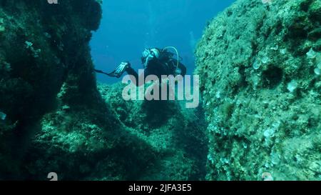 Taucher schwimmen durch einen Riss im Felsen. Riss im Meeresboden über tektonischen Platten. Die Tiktanische Verschiebung der Platten am Meeresgrund. Stockfoto