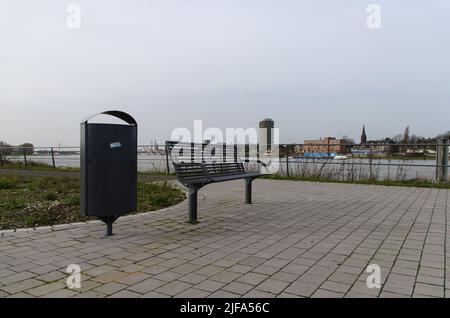 Mülltonne/Mülltonne neben einer Bank am Ufer des Duisburger Ruhrorts, Gemany, mit Industrie und Gebäuden im Hintergrund Stockfoto