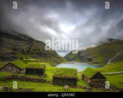 Kleine Häuser in der Nähe eines blauen Sees, ein kleines Haus aus Steinen mit bedecktem Gras am Ufer eines schönen Sees Fiordo de Geiranger, Norwegen Stockfoto