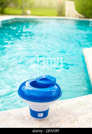 Ein Chlor schwimmt am Rand eines Schwimmbades. Ein Chlorspender für Schwimmbäder mit blauem Wasser im Hintergrund. Dosierschwimmbad zum Schwimmen Stockfoto