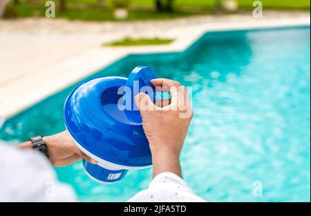 Hände eines Arbeiters, der einen Schwimmer für Chlor in einem Pool installiert, eine Person, die einen Spender für Chlor in einem Pool hält. Hände mit einem Chlorspender für den Pool. Hand eines Stockfoto