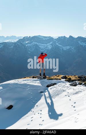 In die Ferne blickender Bergsteiger, neben einer Kairon, vor schneebedeckten Bergen des Rofan, Wanderweg zum Guffert mit erstem Schnee Stockfoto