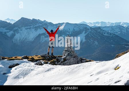 Bergsteiger streckt die Arme in die Luft, neben einer Kairon, vor schneebedeckten Bergen des Rofan, Wanderweg nach Guffert mit First Stockfoto