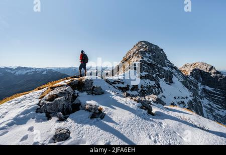 Bergsteiger auf dem felsigen Gipfelgrat mit Herbstschnee, Wanderweg nach Guffert, Sonnenreflex, Brandenberger Alpen, Tirol, Österreich Stockfoto