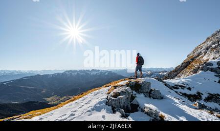 Bergsteiger auf dem felsigen Gipfelgrat mit Herbstschnee, Wanderweg nach Guffert, Sonnenreflex, Brandenberger Alpen, Tirol, Österreich Stockfoto